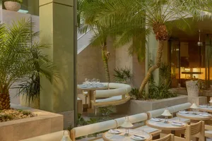 Modern restaurant interior with white walls, green accents, and potted plants, featuring a dining area with tables and chairs