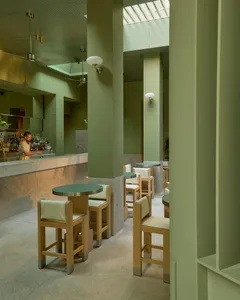 Inviting restaurant interior with green walls, wooden tables, and a bar area, featuring bottles and comfortable seating