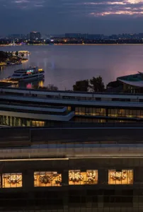 A nighttime view of a building near a large body of water, with lights on the boat and artificial lighting illuminating the windows