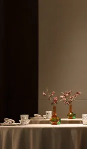 A dining area with a table set for a meal, featuring multiple vases with flowers, utensils, and cups, creating a sophisticated and inviting atmosphere