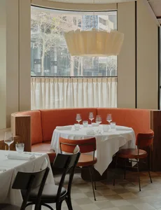 A cozy restaurant dining area with an orange couch, wine glasses, and a dining table surrounded by chairs, set in a warm and inviting atmosphere