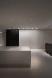 Empty kitchen with white walls and floors, featuring two black cabinets and a clean, minimalistic atmosphere