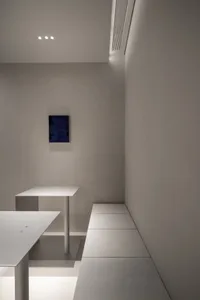 Empty minimalist room with concrete walls, a bench, and two tables, featuring a calm and quiet atmosphere