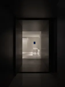 Dark hotel hallway with a black doorway, two tables, and a chair, lacking natural light