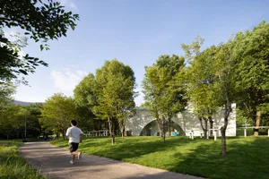 A serene open field with a path for running, surrounded by trees and benches for seating, with a relaxed atmosphere