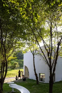 A modern building with a white facade surrounded by trees and several people standing outside, admiring its design or attending an event