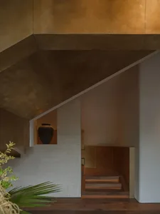 A stone staircase with a wooden railing and a vase at the bottom, set in a larger architectural context