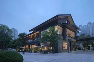 一棟現代建築，地面層擁有大型店面，以黑棕色調混搭，店外有雨傘與盆栽增添溫馨氛圍
