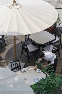 An outdoor dining area with several tables and chairs under large umbrellas, featuring white tablecloths and a clean elegant atmosphere