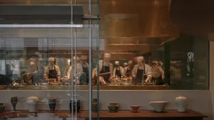 A bustling commercial kitchen with multiple chefs preparing meals, featuring various bowls and cups scattered throughout the area