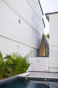 A modern building with a large white wall featuring two windows, one large and one small, made of concrete with a sturdy and solid appearance