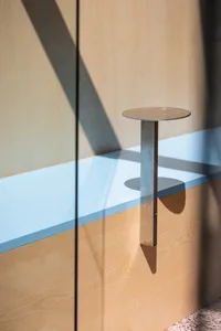 A modern dining space with a wooden table and metal base in front of a glass wall, allowing natural light to create a bright atmosphere