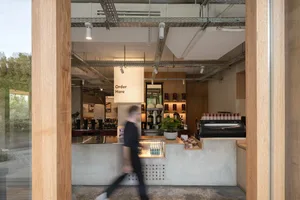 A modern coffee shop interior with a concrete floor, wooden elements, and a casual atmosphere, featuring a man walking past the counter