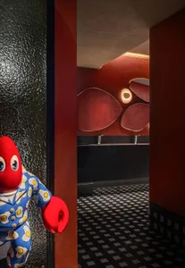 A plush red crab stands in a doorway of a restaurant with a black and white checkered floor