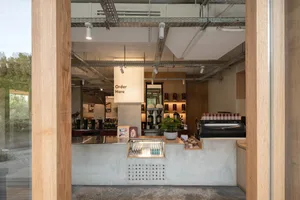 A warm and inviting coffee shop with a rustic atmosphere, featuring a counter, dining table, chairs, potted plants, and various cups and bottles on display