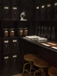 A cluttered room with a wooden table in the center, surrounded by cups, bottles, and other items