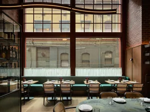 Modern restaurant interior with dining area, tables, chairs, and benches, featuring textured walls and a warm atmosphere