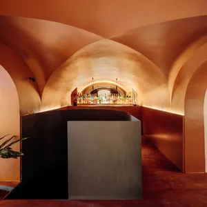 Dimly lit bar area with a long counter, bottles, and wine glasses, surrounded by red-hued walls