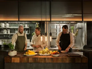 Three men preparing food together in a kitchen with fruits and vegetables on the countertop and several bowls around the space