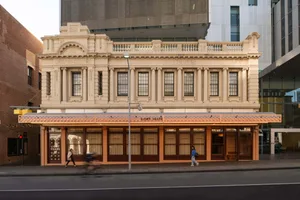 Historic building with intricate details and many windows, set against a city street scene with pedestrians and a bicycle