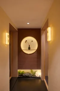 A warm and inviting hallway with a brown wall, a mirror, a vase of flowers, and two lights providing illumination
