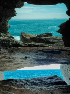 A serene coastal landscape with a grey rocky archway and blue ocean in the background