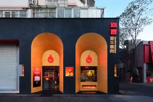 A modern Asian building with a black exterior and arched facade, featuring bottles displayed inside creating a visually interesting effect