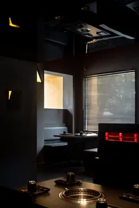 Dark and intimate restaurant interior with concrete walls, multiple chairs and tables, a bar, and two couches