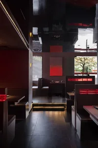 A modern restaurant dining area with multiple tables and chairs, red walls, and warm lighting