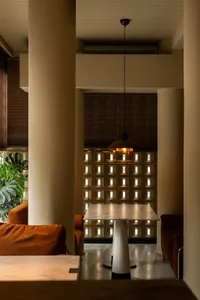 A well-lit living space with a large white table, orange chairs, potted plants, and natural sunlight