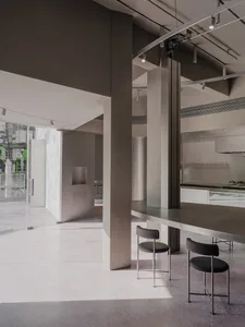 A modern commercial kitchen with a long countertop, chairs, and bottles, featuring ample space for food preparation and dining