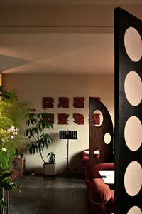A modern living area with a couch, chair, and dining table, surrounded by potted plants and natural light from windows