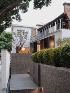 A modern house with a large white exterior wall, two balconies on the second story, and a patio area in front