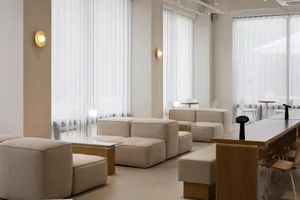 Empty modern living room with white walls, large windows, multiple couches, chairs, and natural light