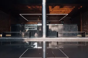Modern bar interior with a black countertop, brick wall, and metal pole, featuring benches and a sophisticated atmosphere