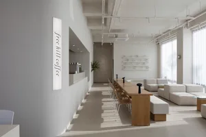 Open living area with white walls and floors, featuring chairs, a dining table, a potted plant, and decorative vases