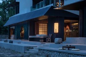 A modern house at night with a stone facade, featuring a kitchen area, dining table, and two benches in an elegant and sophisticated atmosphere