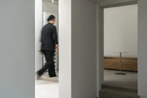 A man walks down a calm and quiet hallway with white walls and two doors, one on each side