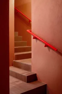 Orange hallway with red handrails, concrete walls, and a staircase leading upwards