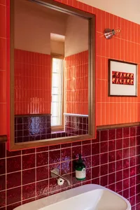 Bathroom with two sinks, red tiles on the walls and floor, and a mirror above one sink, giving off a warm and inviting atmosphere