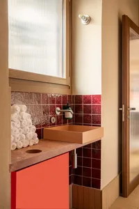 Bathroom with red tiles, an orange sink, and neatly arranged towels, creating a clean and well-maintained atmosphere