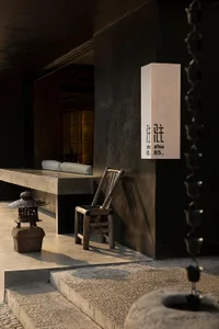 Modern interior space with a black wall, stone bench, and two chairs, featuring a vase and clean lines