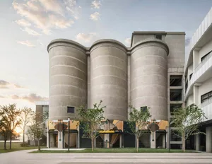 A large building with a modern industrial feel, featuring a circular structure, concrete appearance, and ample natural light from multiple windows