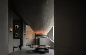 Dimly lit modern room with a circular structure, two chairs, and concrete walls in a black and white color scheme