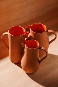 Three stacked brown ceramic pitchers with orange handles sit on a wooden table, adding a pop of color to the space