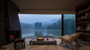 Cozy living area with a wooden table, chairs, and couch, overlooking a lake through a large window
