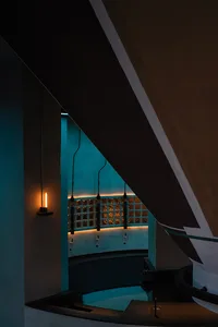 A wooden staircase with a traditional appearance, featuring a wooden railing on both sides, illuminated by two lights, one near the bottom left and another towards the center right