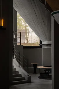 A modern interior space with a staircase, two chairs, a dining table, and natural light from windows
