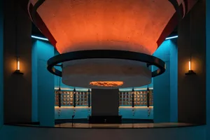 A large stone wall with a circular opening in the center, set against a minimalist industrial backdrop with a sense of depth and dimension