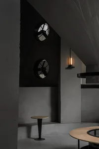 A modern interior design featuring a black wall with two clocks, one round and one square, and two lights, one above the clocks and one further down the wall